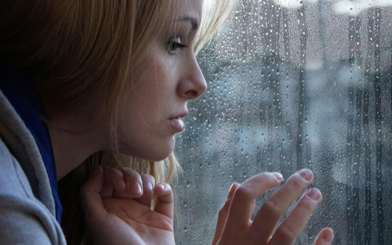 Sad young woman looking through window