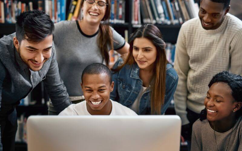 A photo of a group of young students using computers together in a college library