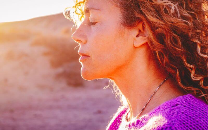 Close-up sunset portrait of attractive woman with closed eyes and sun in the background.