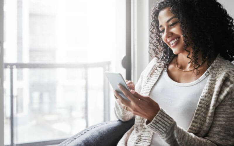 Image of a happy young woman relaxing while texting on her mobile phone at home during the day