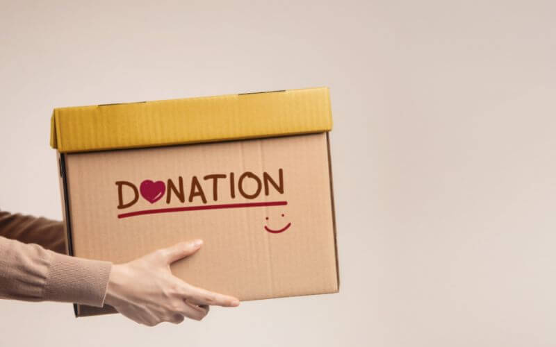 Woman donation concept with box of items for donation with donation label, smile and heart.
