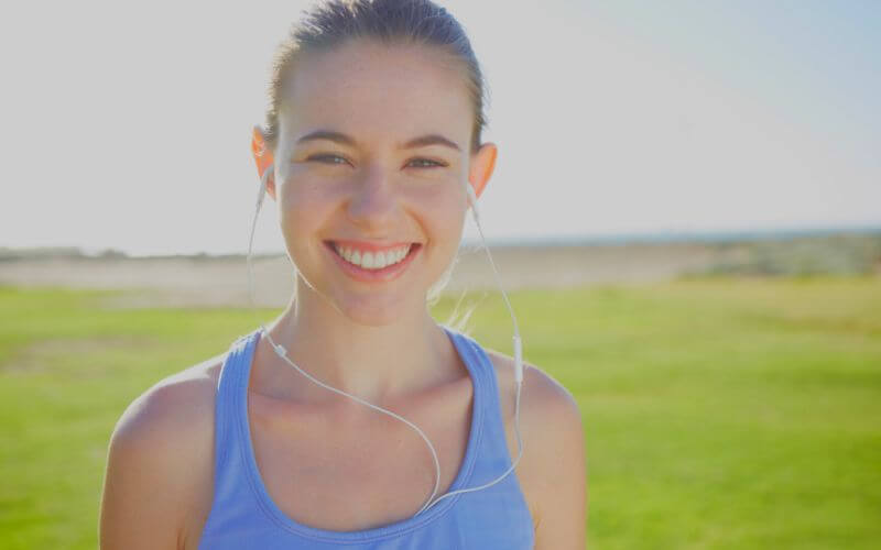 A happy young woman standing outdoors wearing earphones