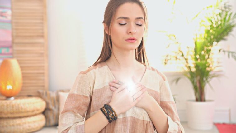 A young and attractive woman putting her hand on her heart representing heart chakra affirmations